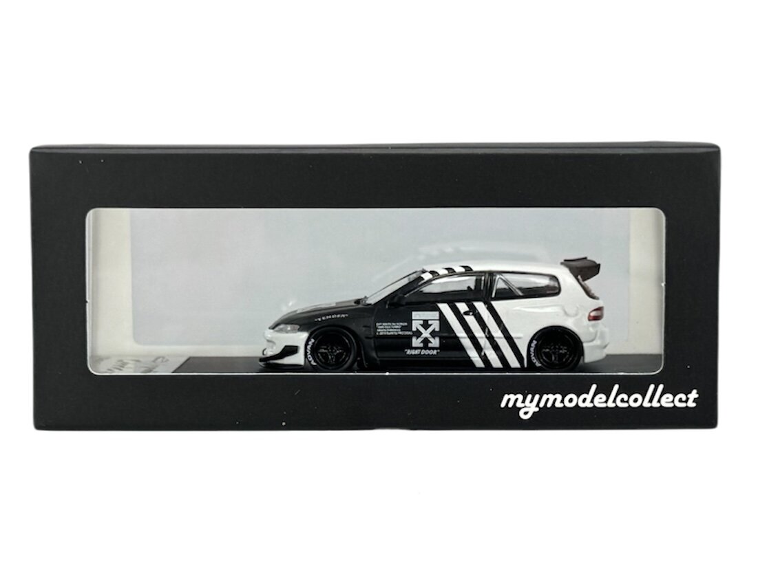 Model samochodu w skali 1:64 w kolorze czarno-białym, umieszczony w czarnym pudełku z przezroczystym frontem. Na pudełku widnieje napis \'mymodelcollect\'.