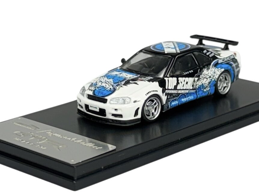 Model samochodu w skali 1:64 z detalami w kolorach białym, czarnym i niebieskim, z napisem \'TOP SECRET\' na boku. Model umieszczony jest na czarnej podstawce z metalową tabliczką.