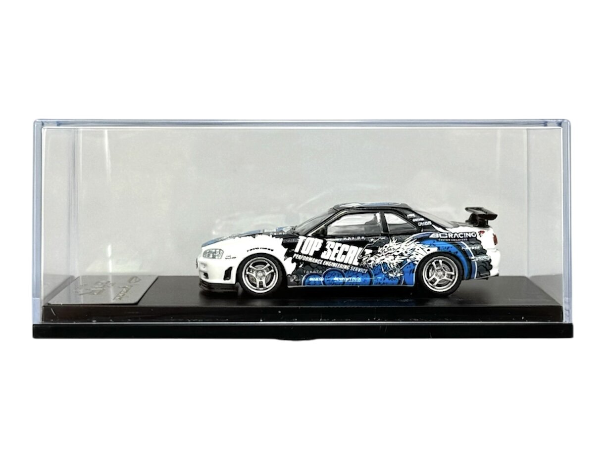 Model samochodu w skali 1:64 przedstawia sportowy pojazd z napisem \'TOP SECRET\' na boku, umieszczony w przezroczystej gablocie na czarnej podstawce.