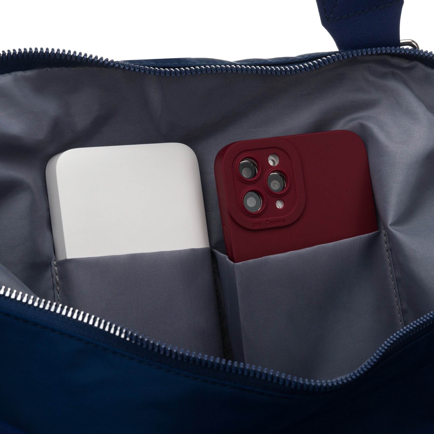 Wnętrze granatowej torby z szarym materiałem, zawierające dwa przedmioty: biały prostokątny obiekt i czerwony telefon z trzema obiektywami aparatu.
