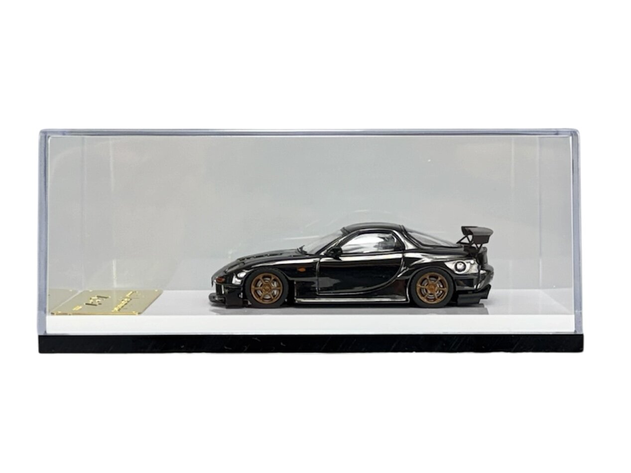 Model samochodu w skali 1:64 w kolorze ciemnym, umieszczony w przezroczystej gablocie. Obok modelu znajduje się złota tabliczka z napisem \'My Model\'.