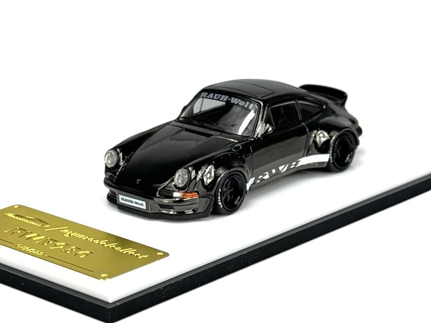 Model samochodu w kolorze czarnym z napisem \'RAUH-Welt\' na przedniej szybie, umieszczony na białej podstawce z metalową tabliczką. Na tabliczce widnieje napis \'RWB 930\'.