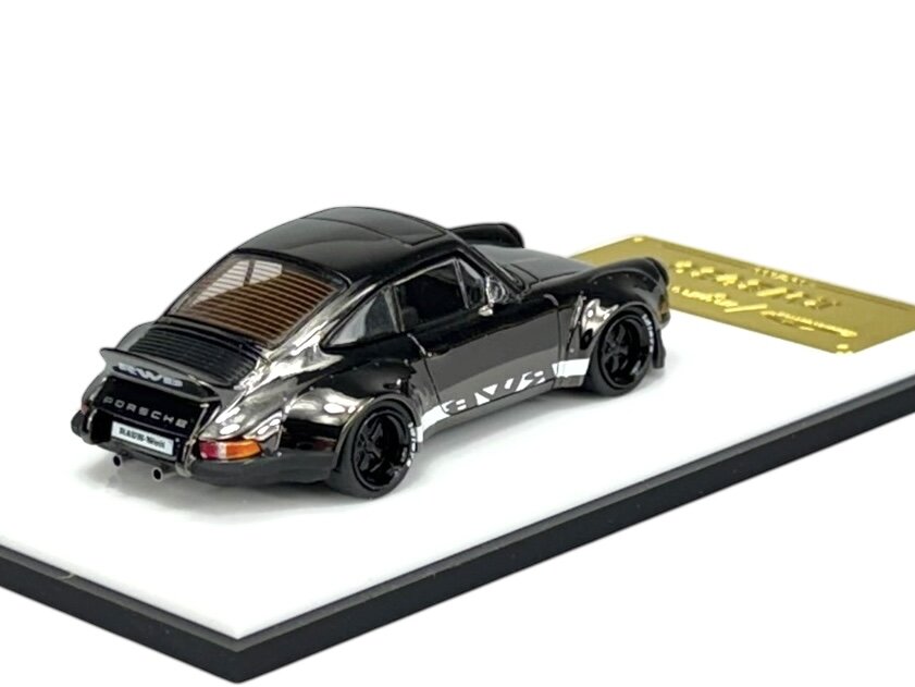 Model samochodu w kolorze ciemnym z napisem \'Porsche\' na tylnej części. Obok znajduje się złota tabliczka z napisem \'Rauh-Welt\'.
