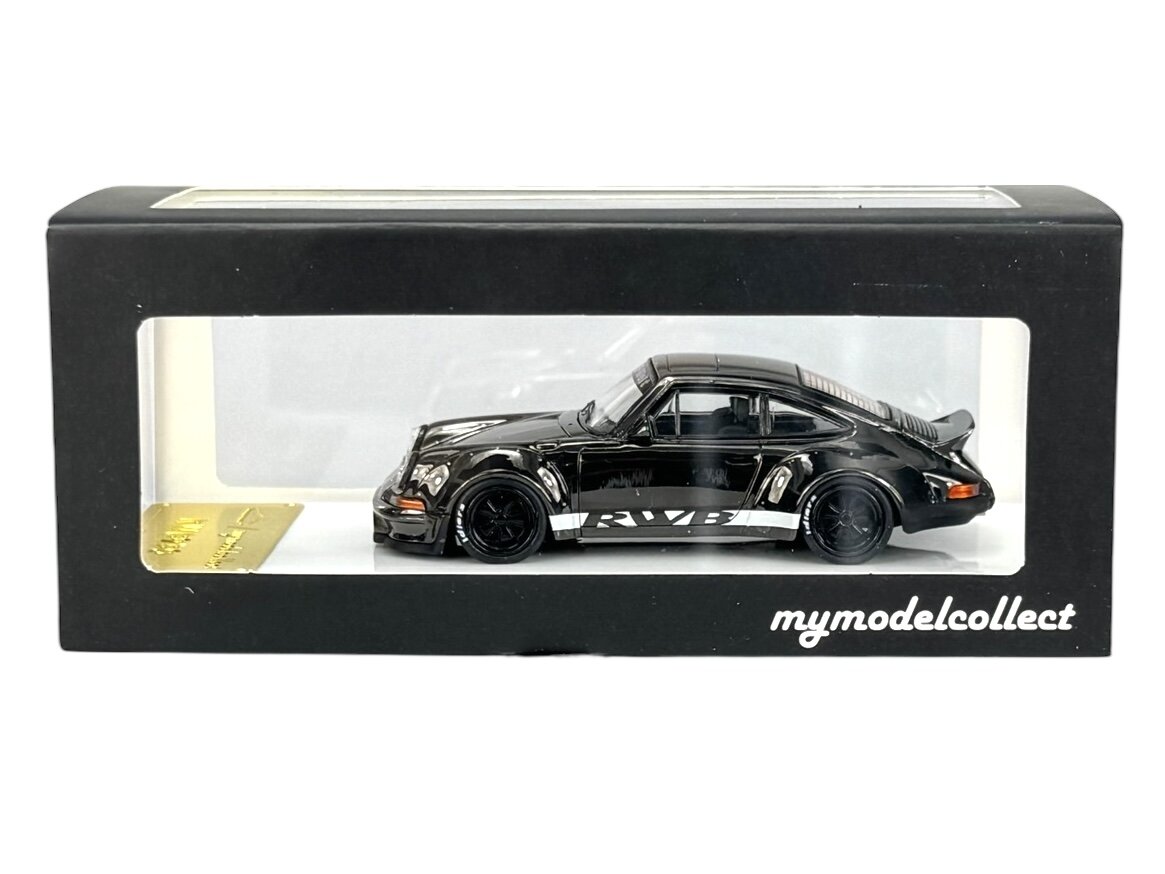 Model samochodu w skali 1:64 w kolorze ciemnym, umieszczony w czarnym pudełku z przezroczystym okienkiem. Na pudełku widnieje napis \'mymodelcollect\'.