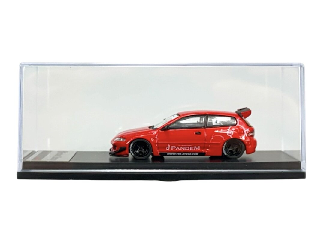 Czerwony model samochodu w skali 1:64 umieszczony w przezroczystej gablocie. Na boku pojazdu widoczny jest napis \'Pandem\'.