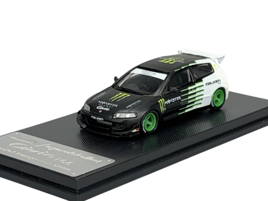 Model samochodu w skali 1:64 przedstawia czarno-biały pojazd z zielonymi felgami i napisami \'Monster\' oraz \'Falken\'. Samochód umieszczony jest na czarnej podstawce z napisem \'Civic EG6 Rocket Bunny\'.