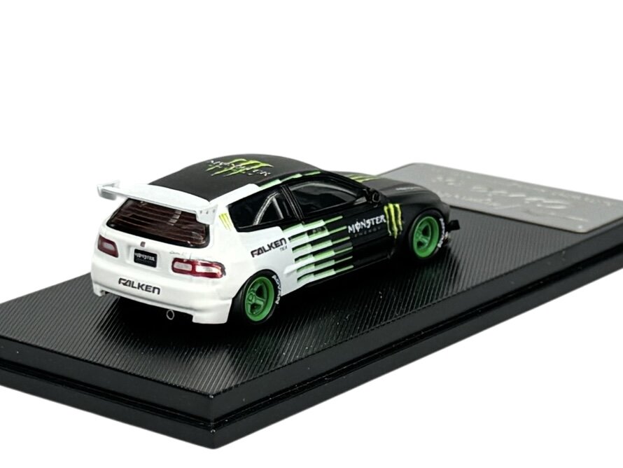 Model samochodu w skali 1:64 przedstawia czarno-biały pojazd z zielonymi felgami, umieszczony na czarnej podstawce. Na samochodzie widoczne są logotypy \'Falken\' i \'Monster\'.
