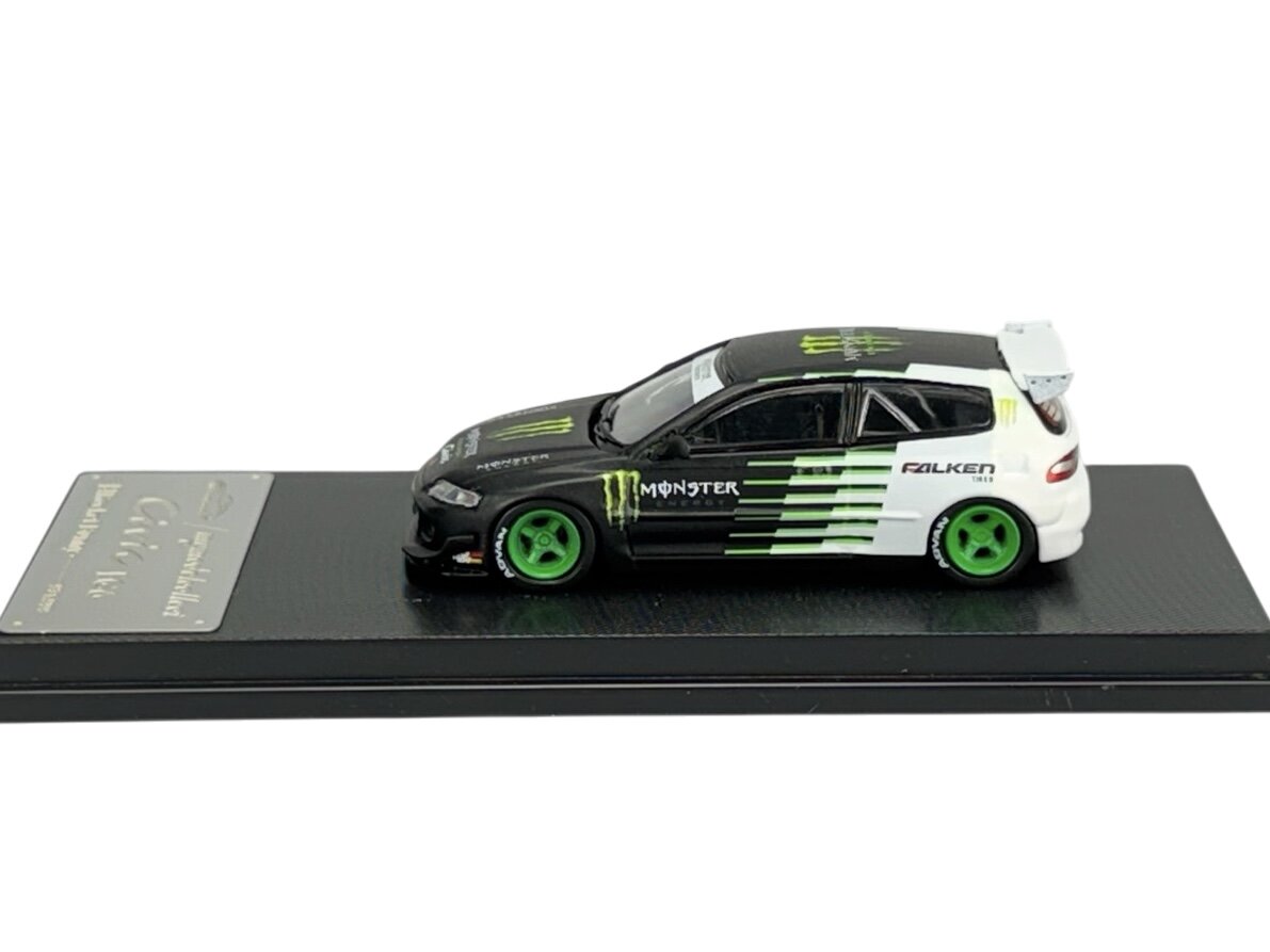 Model samochodu w skali 1:64 w kolorach czarnym i białym z zielonymi felgami, umieszczony na czarnej podstawce. Na karoserii widoczne są logotypy \'Monster\' i \'Falken\'.