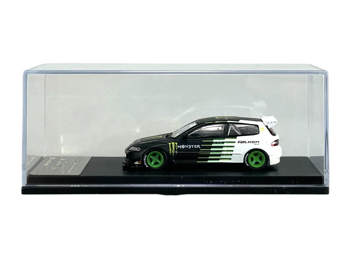 Model samochodu w skali 1:64 w kolorach czarnym i białym z zielonymi felgami, umieszczony w przezroczystej gablocie. Na boku widoczne są logotypy \'Monster\' i \'Falken\'.