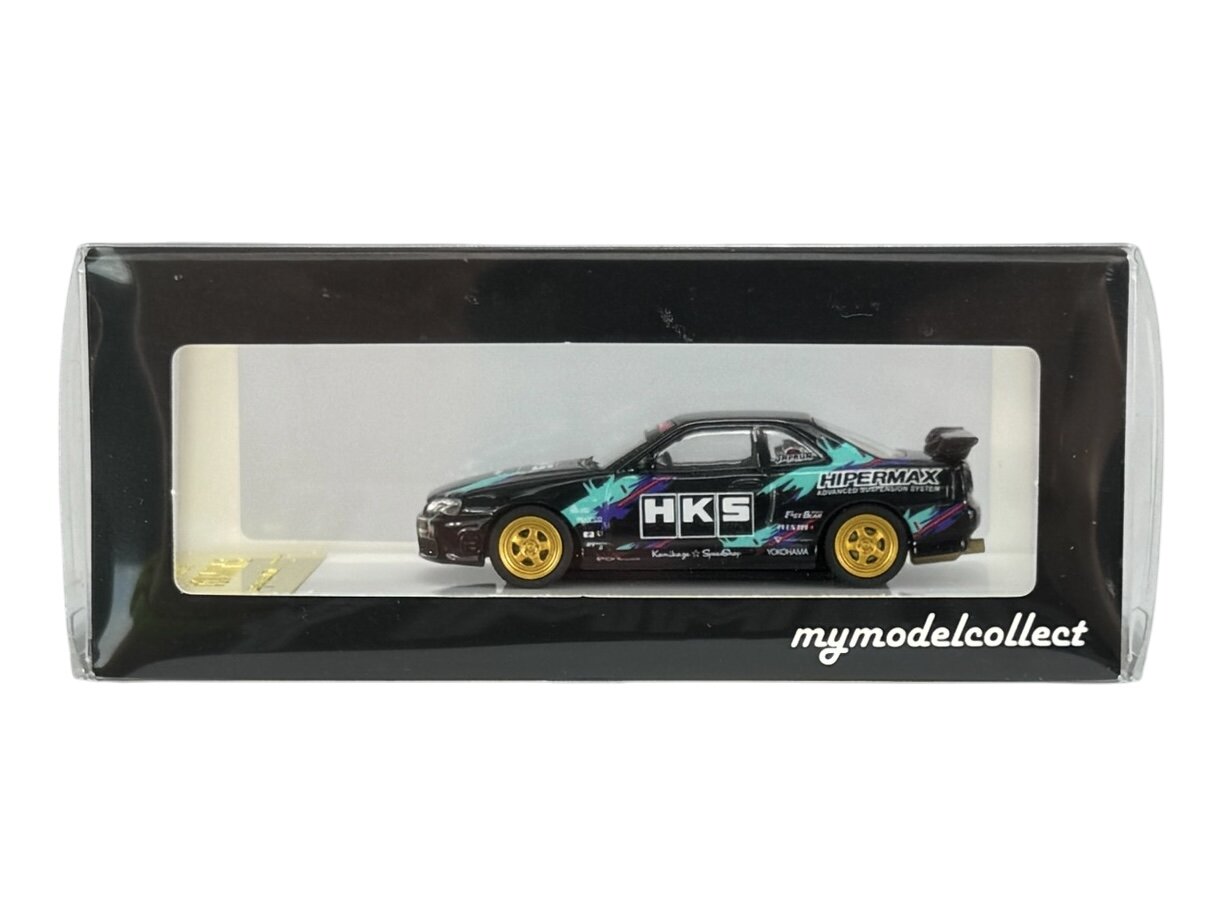 Model samochodu w skali 1:64 w opakowaniu z przezroczystym frontem, z widocznym napisem \'HKS\' na boku pojazdu. Na opakowaniu znajduje się napis \'mymodelcollect\'.