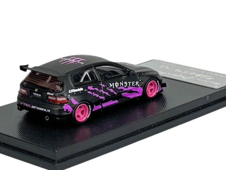 Model samochodu w skali 1:64 w kolorze czarno-fioletowym z różowymi felgami, umieszczony na czarnej podstawce. Na karoserii widoczne są napisy \'MONSTER\' oraz \'VTEC just kicked in yo\'.