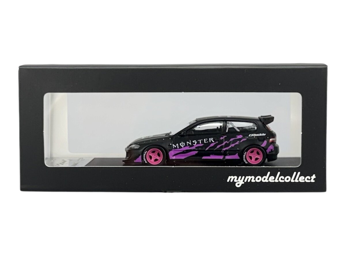 Model samochodu w skali 1:64 w kolorze czarno-fioletowym z napisem \'MONSTER\' na boku, umieszczony w czarnym pudełku z przezroczystym frontem. Na pudełku widnieje napis \'mymodelcollect\'.
