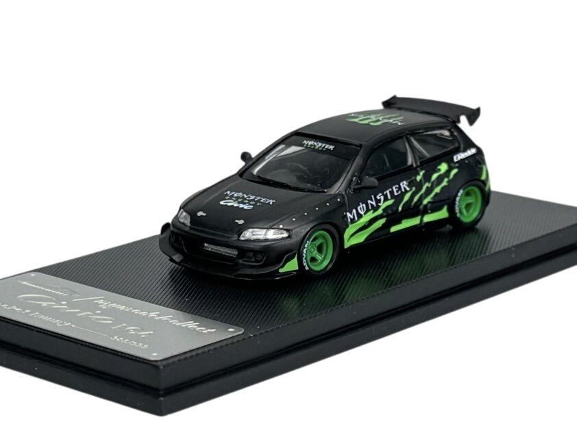 Model samochodu w skali 1:64, czarny z zielonymi akcentami i napisami \'MONSTER\' oraz \'NENOTEX\'. Pojazd umieszczony jest na czarnej podstawce z napisem \'Civic Eg6 Rocket Bunny\'.
