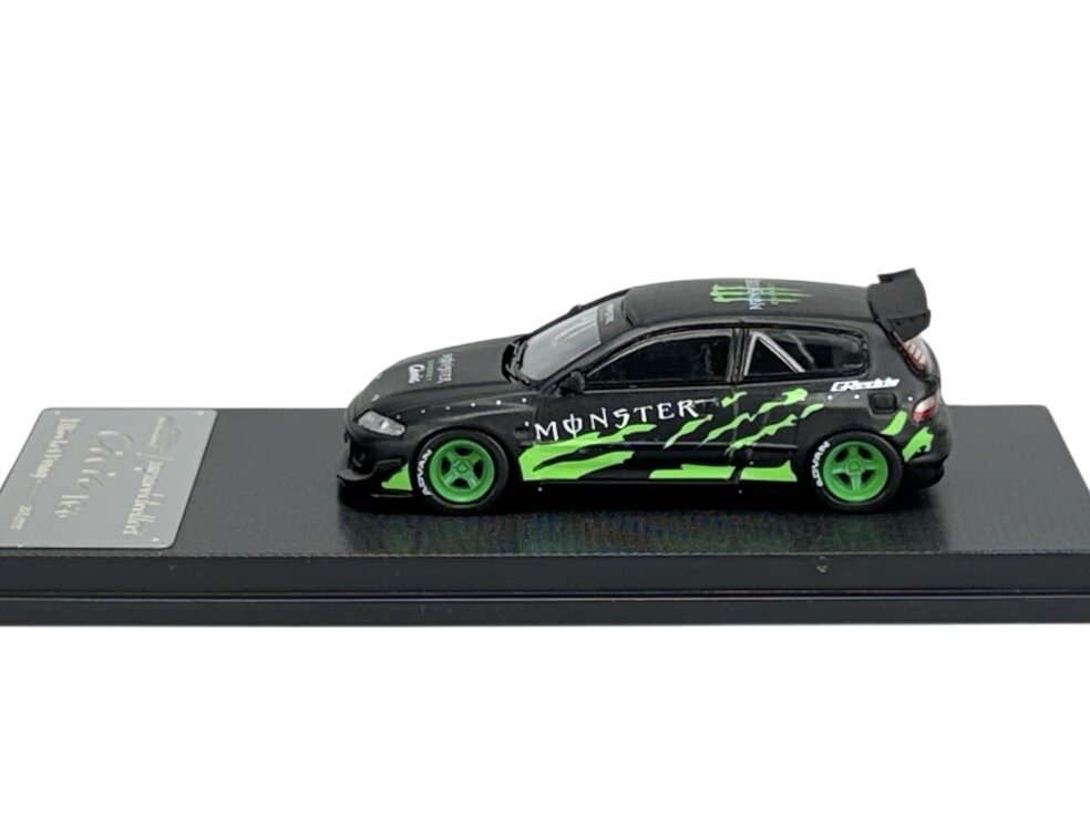 Model samochodu w skali 1:64, czarny z zielonymi akcentami i napisem \'MONSTER\' na boku, umieszczony na czarnej podstawce. Koła są zielone, a na dachu widoczne jest logo w zielonym kolorze.