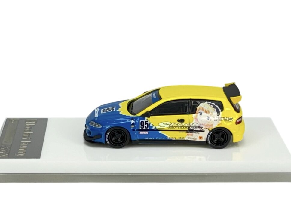 Model samochodu w skali 1:64 w kolorach żółtym i niebieskim z numerem 95 oraz grafiką postaci na boku. Na podstawce widoczny napis \'Rocket Bunny\'.