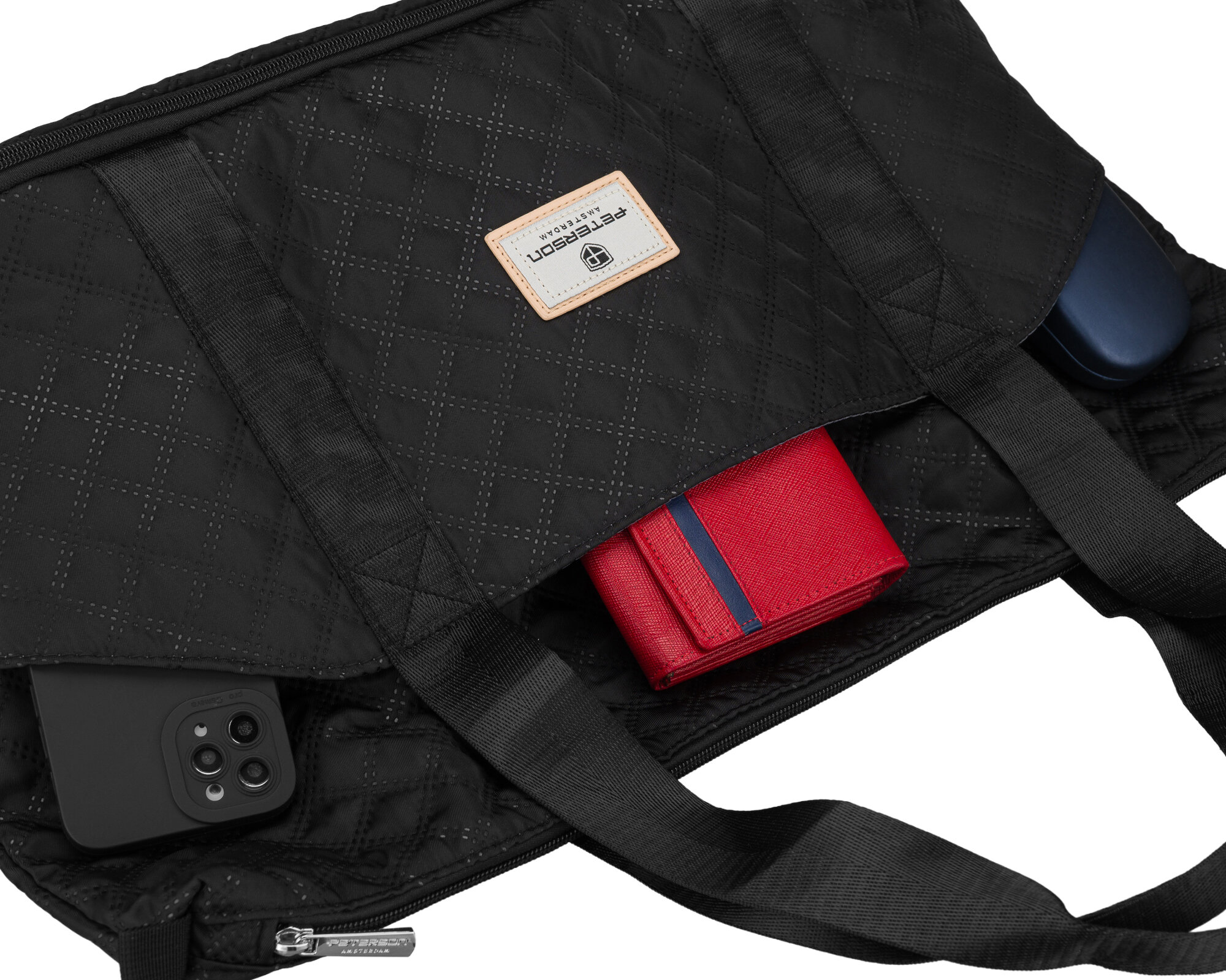 Czarna, pikowana torba z widocznym logo \'Peterson\' na naszywce. W torbie znajdują się czerwony portfel, czarne etui na telefon i niebieskie etui.