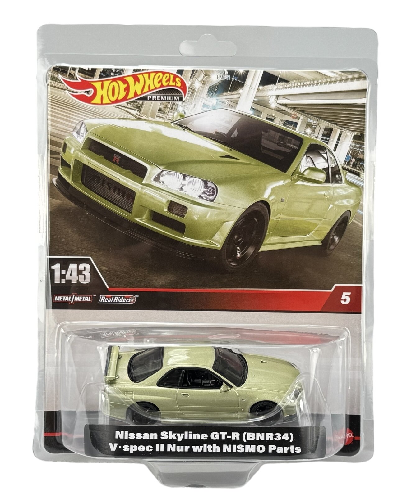 Opakowanie z modelem samochodu Hot Wheels przedstawiające zielony Nissan Skyline GT-R (BNR34) V-spec II Nur z częściami NISMO w skali 1:43. Na opakowaniu widnieje logo Hot Wheels Premium oraz napis \'Metal/Metal\' i \'Real Riders\'.