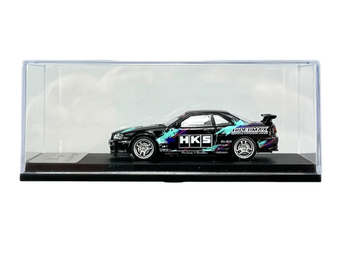 Model samochodu w skali 1:64 umieszczony w przezroczystej gablocie. Na boku pojazdu widoczne są napisy \'HKS\' i \'HIPERMAX\'.