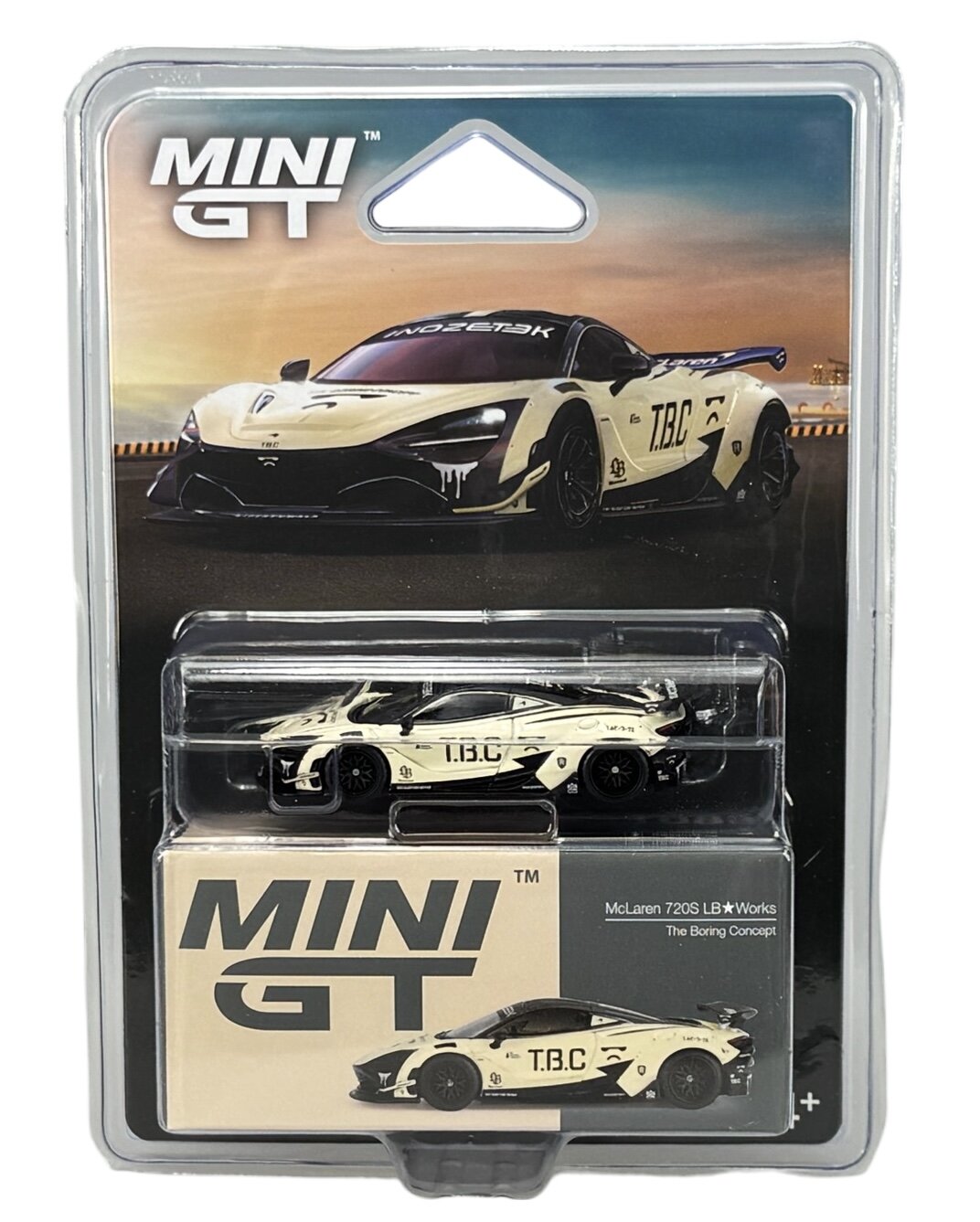 Opakowanie z modelem samochodu Mini GT w kolorze beżowym, z widocznym napisem \'T.B.C\' na boku. Na opakowaniu znajduje się również logo \'MINI GT\' oraz napis \'McLaren 720S LB★Works The Boring Concept\'.