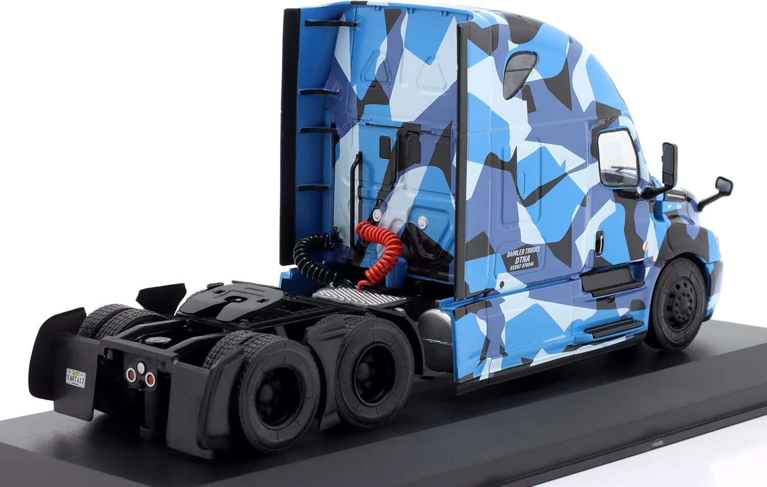 Model ciężarówki w skali 1:43 w kolorze niebieskim z kamuflażowym wzorem, umieszczony na czarnej podstawce. Na tylnej części kabiny widoczne są czerwone i czarne przewody.