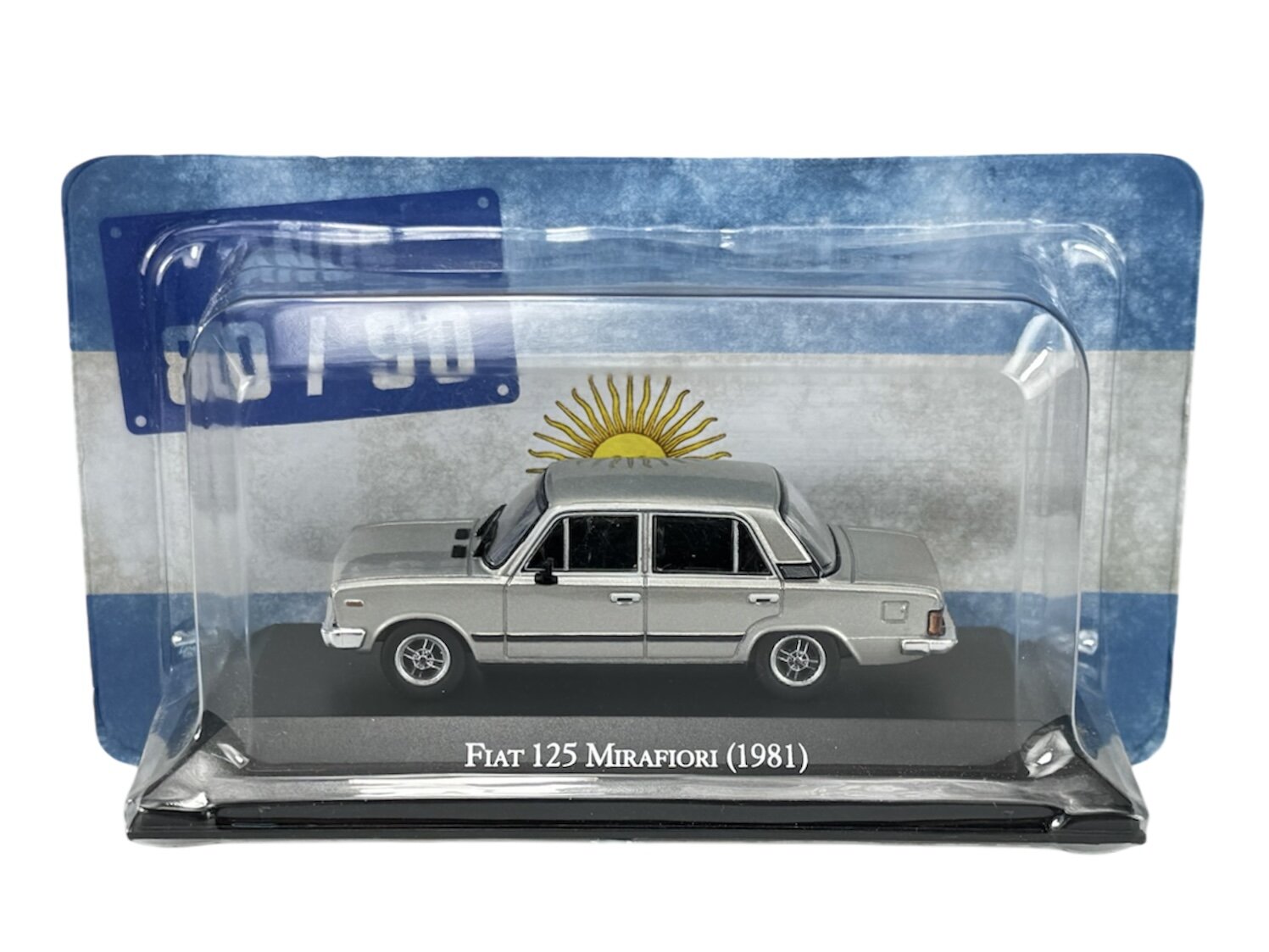 Model samochodu Fiat 125 Mirafiori (1981) w skali 1:43 w srebrnym kolorze, zapakowany w przezroczyste opakowanie z tłem przedstawiającym flagę z słońcem. Na podstawce widoczny jest napis \'Fiat 125 Mirafiori (1981)\'.