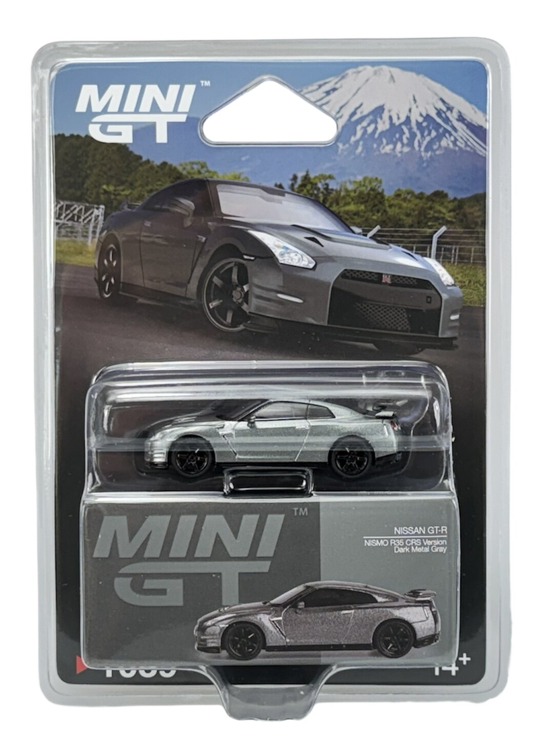 Opakowanie z modelem samochodu w skali 1:64, przedstawiające srebrny Nissan GT-R Nismo R35. Na opakowaniu widnieje napis \'MINI GT\' oraz zdjęcie pełnowymiarowego samochodu na tle górskiego krajobrazu.