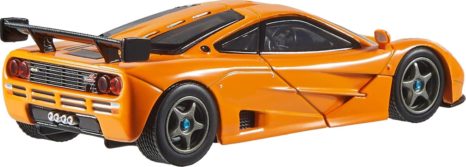 Model samochodu w skali 1:43, przedstawiający pomarańczowy pojazd sportowy z dużym tylnym spojlerem i szczegółowymi felgami. Samochód ma czarne detale i widoczne tylne światła.