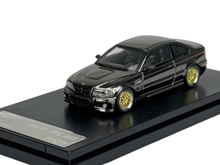 Model samochodu w kolorze ciemnym z żółtymi felgami, umieszczony na czarnej podstawce z napisem \'BMW E46 M3\'.