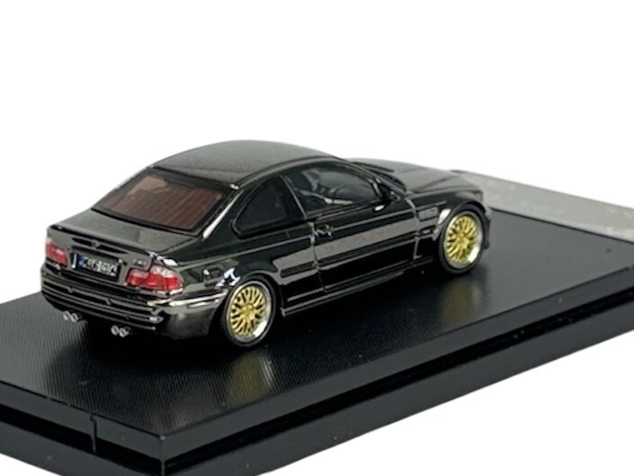 Model samochodu w skali 1:64 przedstawiający BMW M3 E46 w kolorze ciemnym z chromowanymi elementami i złotymi felgami, umieszczony na czarnej podstawce. Widoczne są detale takie jak tylne światła i podwójny wydech.