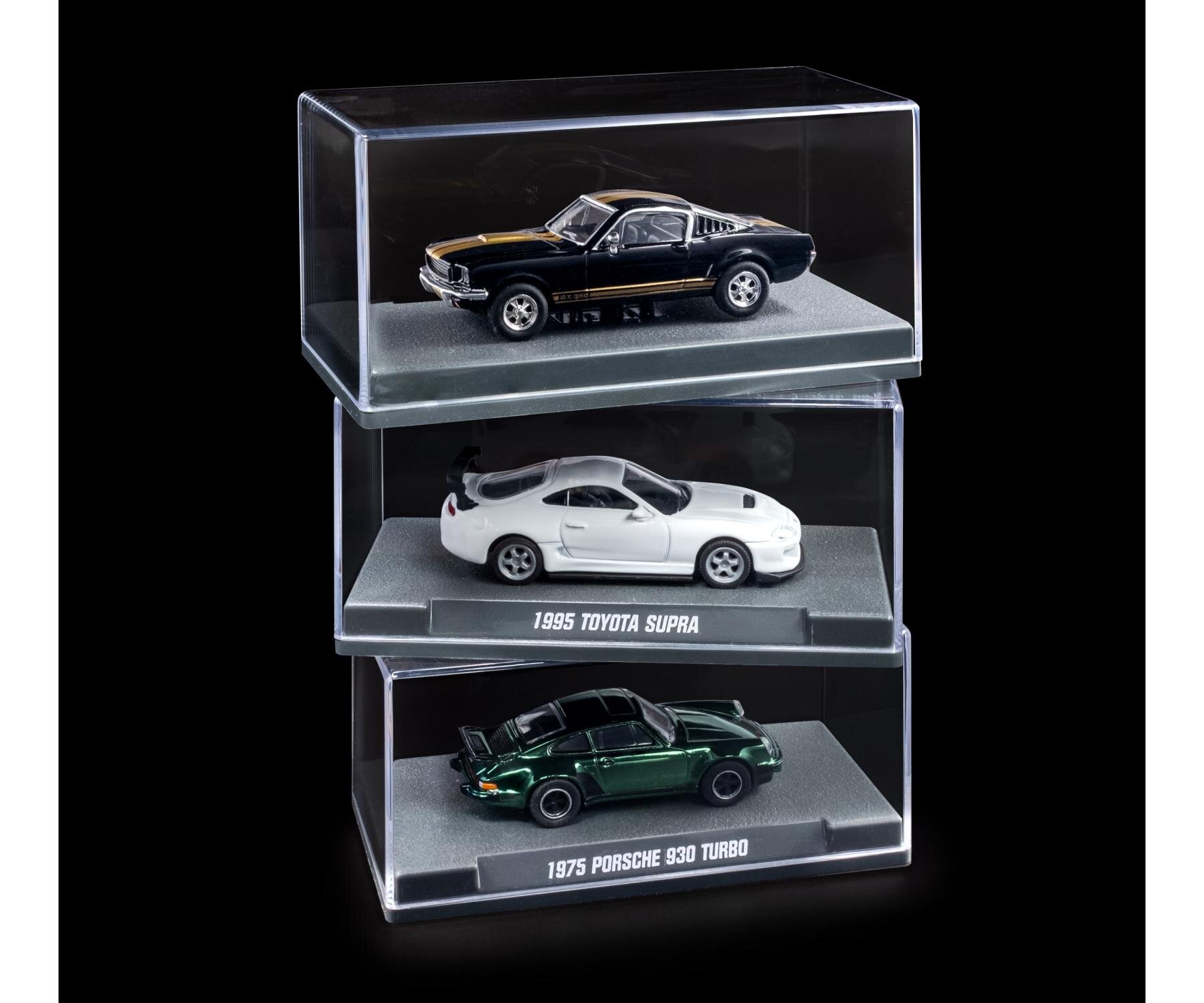 Trzy modele samochodów w skali 1:64 umieszczone w przezroczystych gablotach. Widoczne napisy to: \'1995 TOYOTA SUPRA\' i \'1975 PORSCHE 930 TURBO\'.