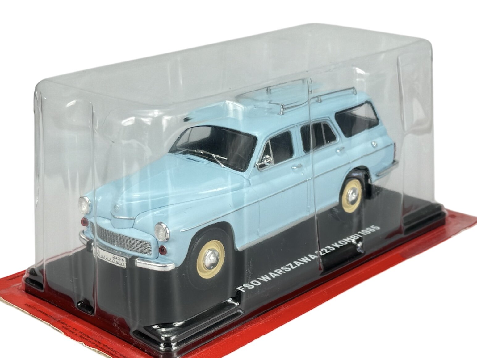 Model samochodu FSO Warszawa 223 Kombi 1965 w kolorze niebieskim, umieszczony w przezroczystym opakowaniu na czerwonej podstawce. Na podstawce widoczny jest napis \'FSO WARSZAWA 223 KOMBI 1965\'.
