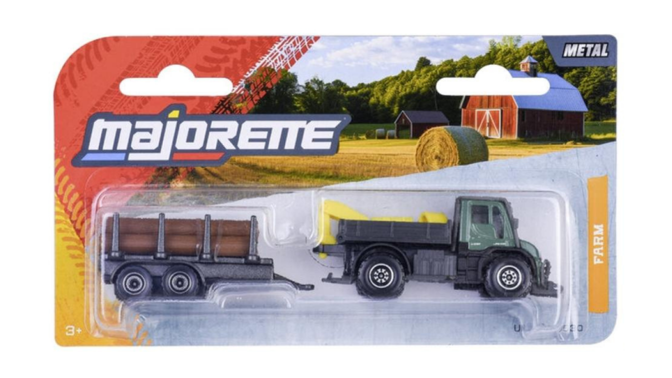 Opakowanie z metalowym modelem pojazdu Majorette Farm Unimog U530 z przyczepą na drewno, na tle wiejskiego krajobrazu z belą siana i stodołą. Widoczne napisy: \'majorette\', \'METAL\', \'FARM\'.