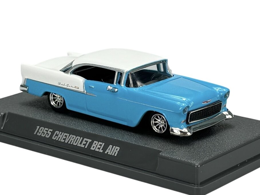 Model samochodu 1955 Chevrolet Bel Air w kolorze niebieskim z białym dachem, umieszczony na podstawce z napisem \'1955 CHEVROLET BEL AIR\'.