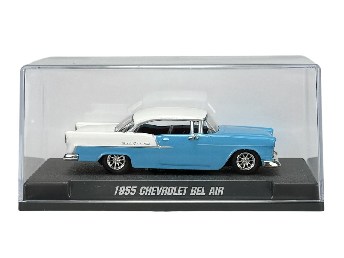 Model samochodu 1955 Chevrolet Bel Air w kolorze niebieskim z białym dachem, umieszczony w przezroczystej gablocie. Na podstawce widnieje napis \'1955 CHEVROLET BEL AIR\'.