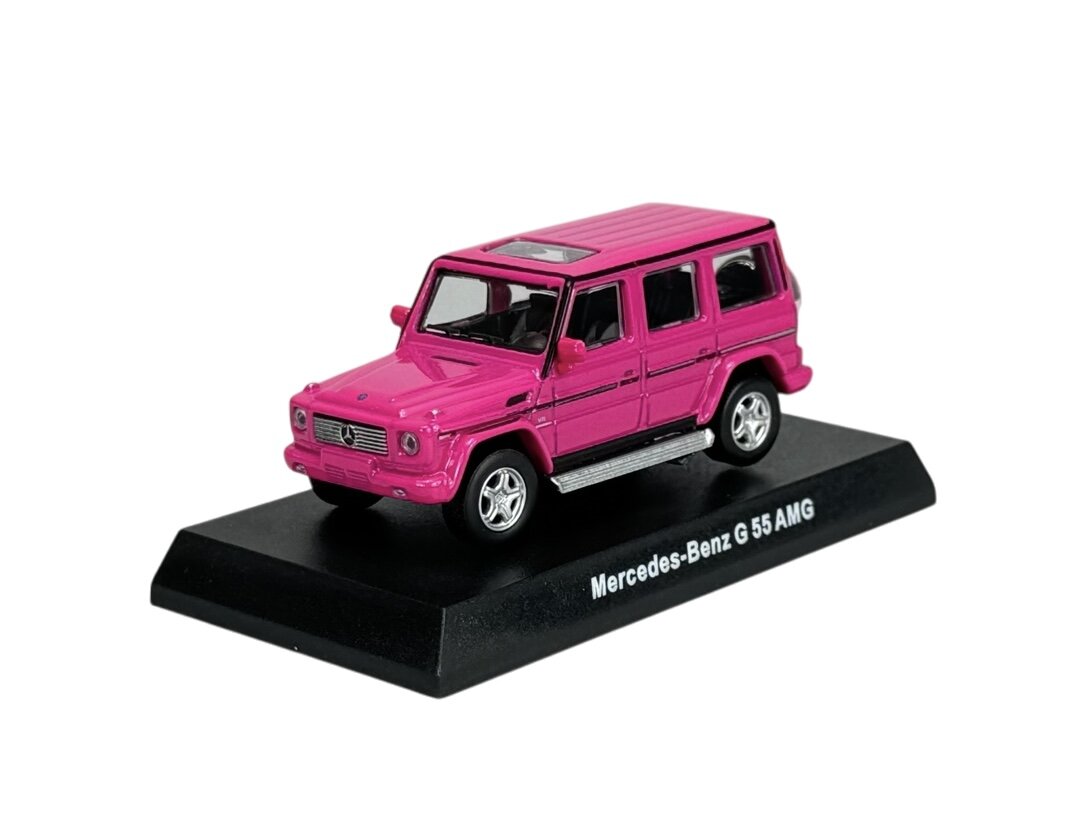 Różowy model samochodu Mercedes-Benz G 55 AMG w skali 1:64 umieszczony na czarnej podstawce. Na podstawce widoczny jest napis \'Mercedes-Benz G 55 AMG\'.