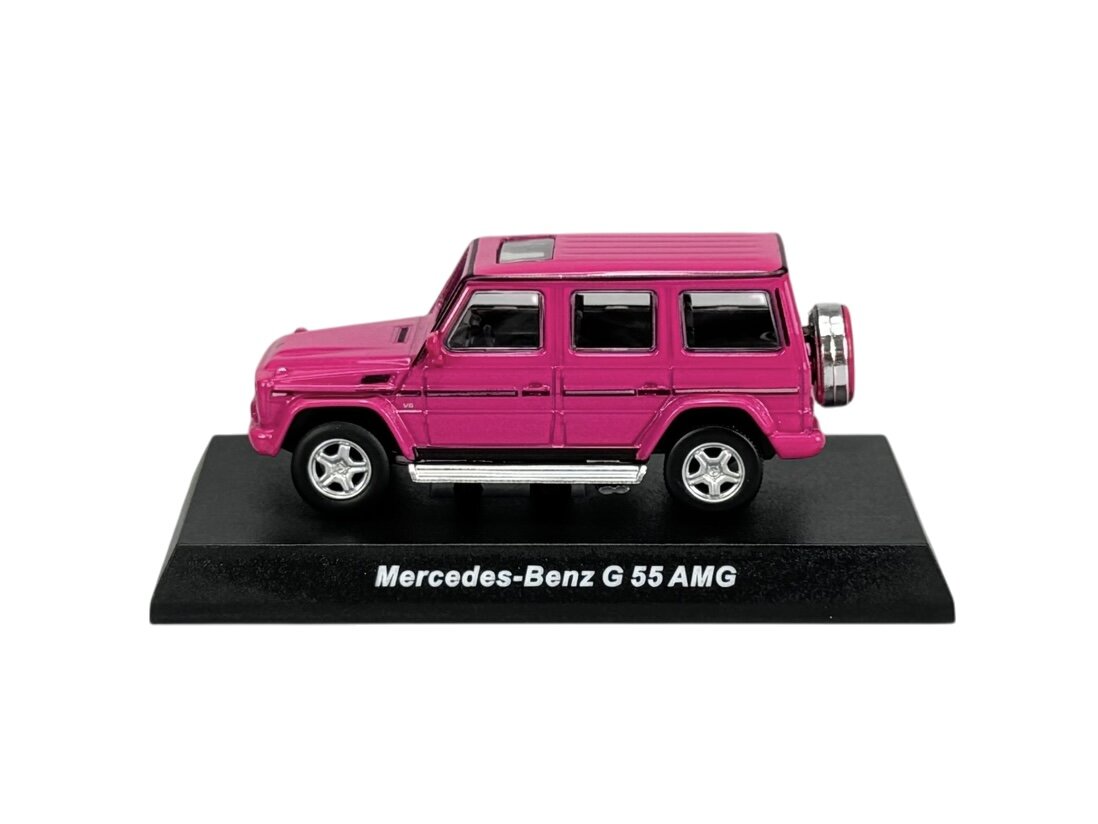 Różowy model samochodu Mercedes-Benz G 55 AMG w skali 1:64, umieszczony na czarnej podstawce z napisem \'Mercedes-Benz G 55 AMG\'.