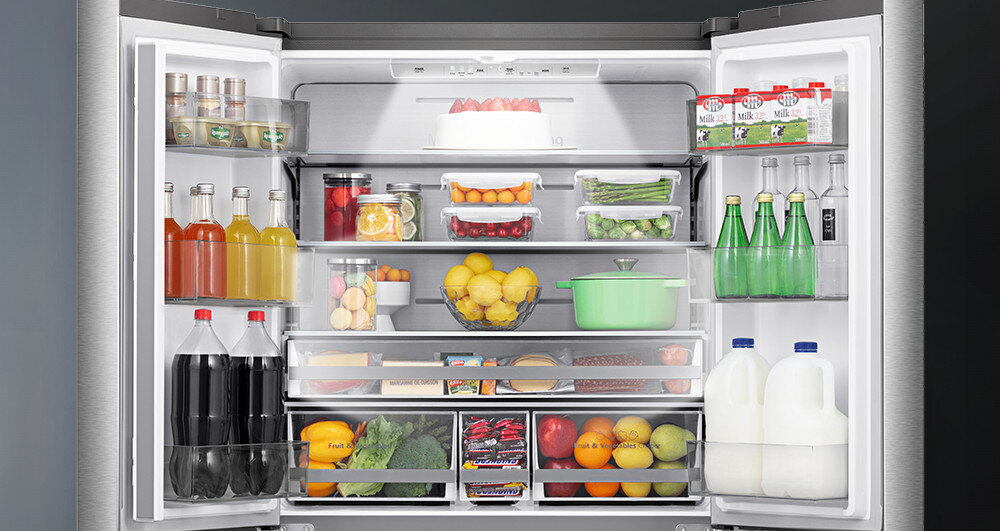 Otwarta lodówka z różnorodnymi produktami spożywczymi, w tym napojami, owocami, warzywami i nabiałem. Wnętrze jest dobrze zorganizowane z półkami i szufladami na różne produkty.