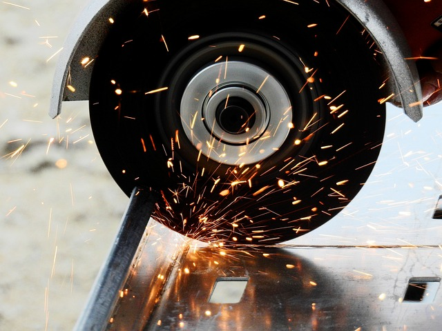 Obraz przedstawia tarczę korundową przecinającą metal, z której sypią się iskry. Tarcza jest zamontowana w przecinarce, a metalowa powierzchnia ma prostokątne otwory.