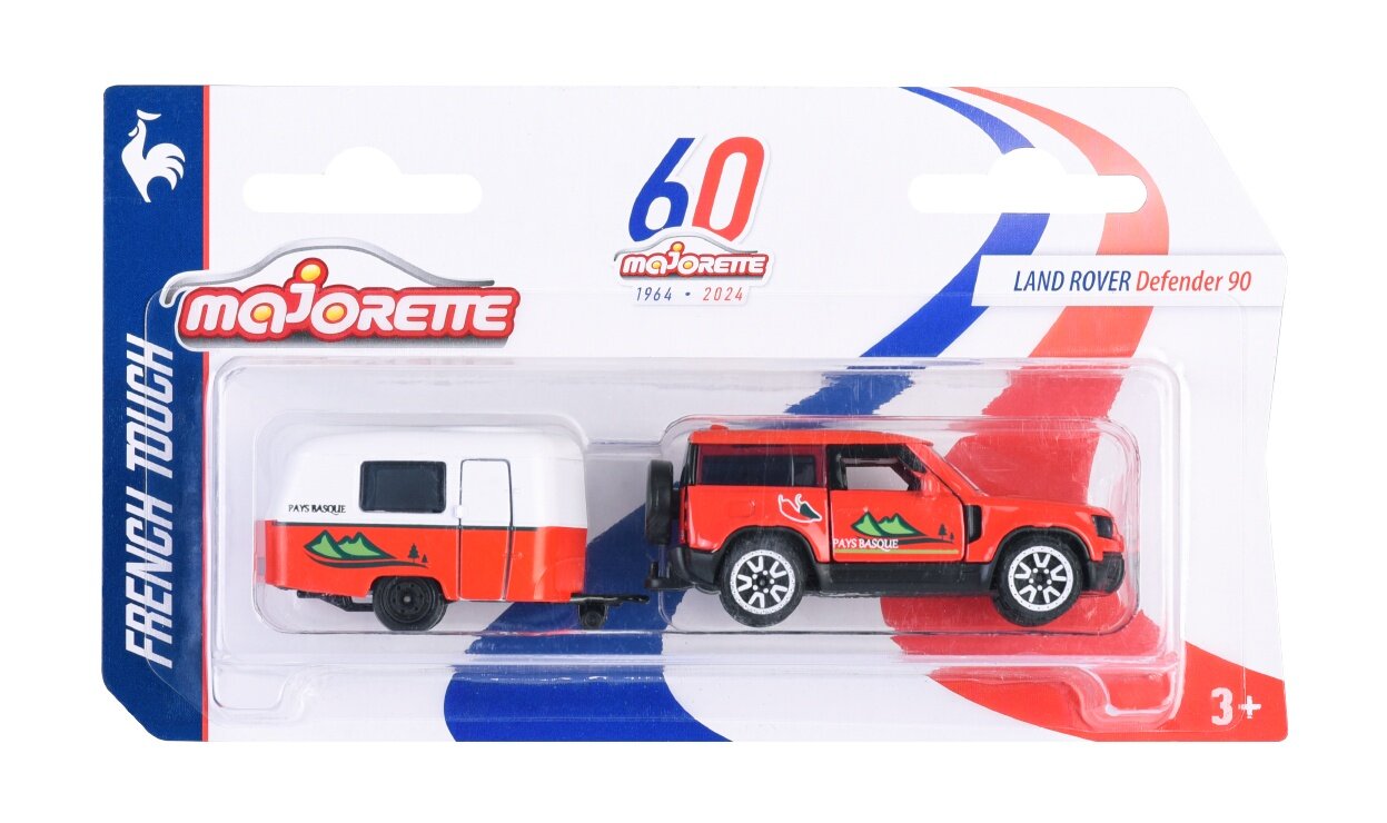 Opakowanie zawiera metalowy model Land Rover Defender 90 z przyczepą w skali 1:64, w kolorze czerwonym z grafiką gór. Na opakowaniu widnieje logo \'majorette\' oraz napis \'FRENCH TOUCH\'.