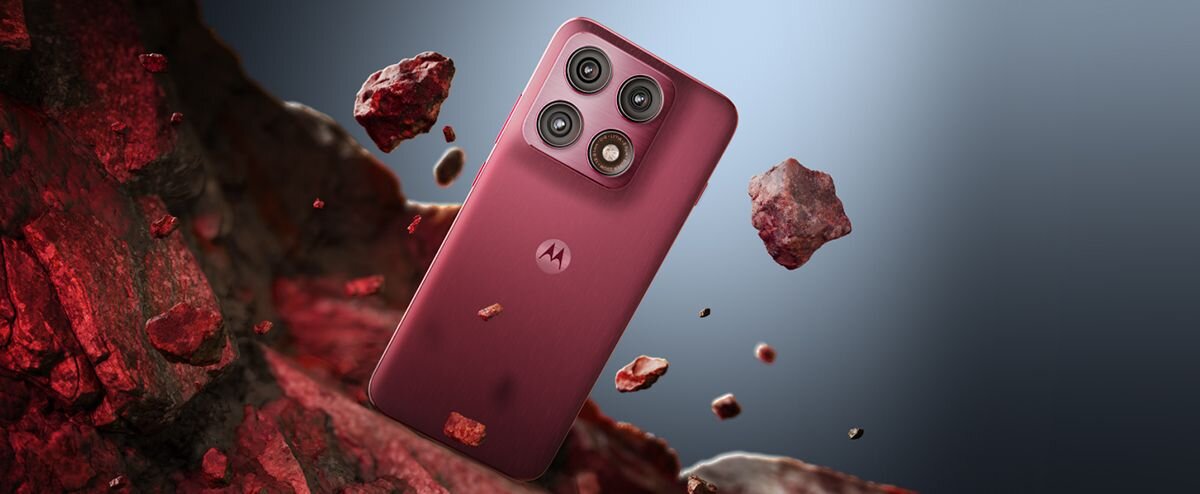Smartfon w kolorze czerwonym z trzema aparatami na tylnej obudowie, otoczony unoszącymi się kawałkami skał. Na obudowie widoczne jest logo producenta w formie litery M.