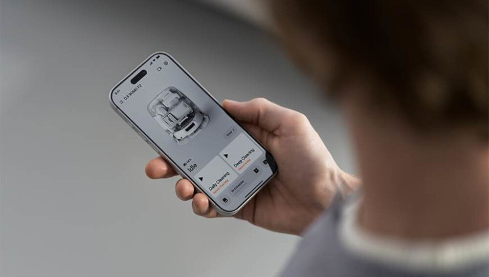 Osoba trzyma smartfon z aplikacją pokazującą obraz robota sprzątającego i opcje sterowania. Na ekranie widoczny jest tekst: \'DJI Romo P2\'.