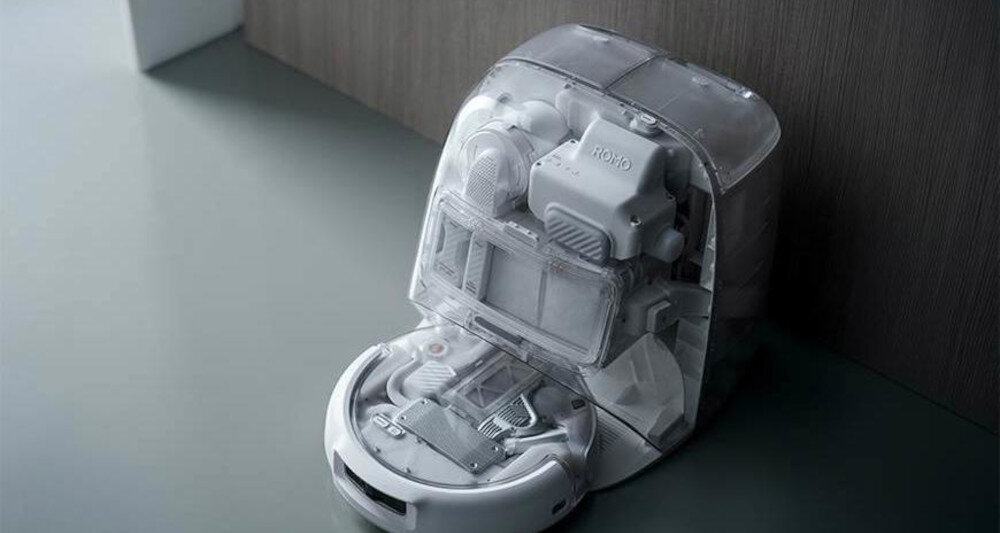 Przezroczysty robot sprzątający z widocznymi wewnętrznymi mechanizmami, na obudowie napis \'ROMO\'.