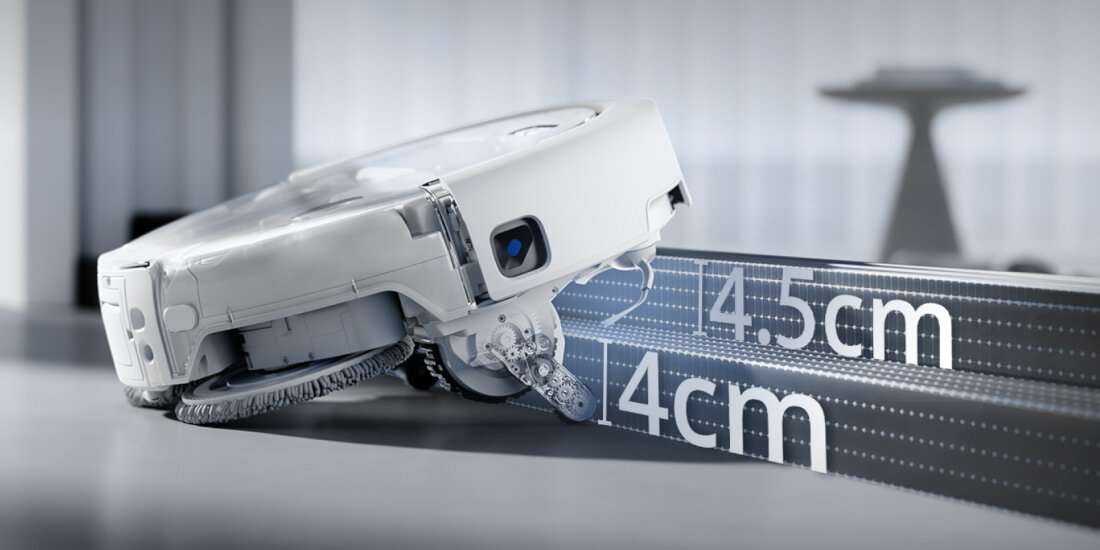 Robot sprzątający pokonuje przeszkodę o wysokości 4,5 cm. Obok widoczna jest miarka z oznaczeniami 4 cm i 4,5 cm.