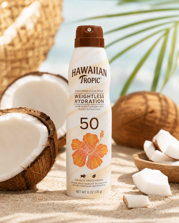 Na obrazie znajduje się spray do opalania marki Hawaiian Tropic z napisem \'Weightless Hydration 50\'. W tle widoczne są połówki kokosa i fragmenty liści palmowych na piasku.