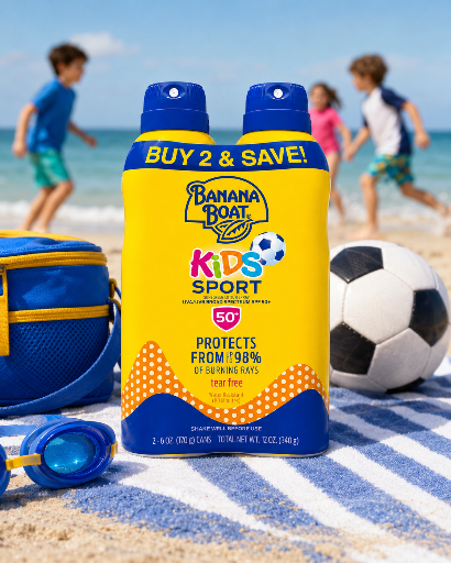 Na plaży znajduje się żółta butelka Banana Boat Kids Sport SPF 50 z napisem \'BUY 2 & SAVE!\', obok piłki nożnej i niebieskich okularów pływackich. W tle bawią się dzieci.
