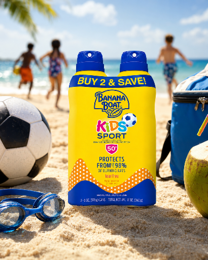Na plaży znajduje się żółta butelka Banana Boat Kids Sport SPF 50 z napisem \'BUY 2 & SAVE!\'. W tle widać dzieci bawiące się na piasku oraz piłkę i okulary do pływania.