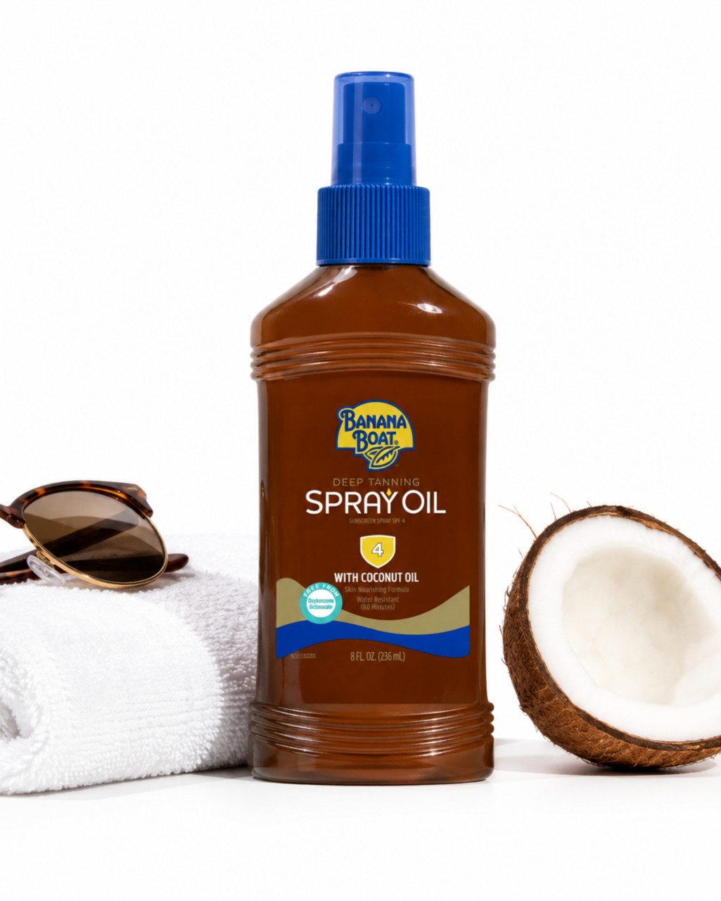 Brązowa butelka z niebieskim dozownikiem, oznaczona jako \'Banana Boat Deep Tanning Spray Oil 4 With Coconut Oil\', stoi obok białego ręcznika, okularów przeciwsłonecznych i połówki kokosa.