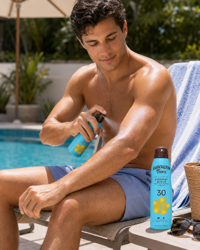 Mężczyzna siedzi przy basenie i aplikuje spray do opalania na ramię. Obok niego stoi butelka sprayu z napisem \'HAWAIIAN TROPIC 30\'.
