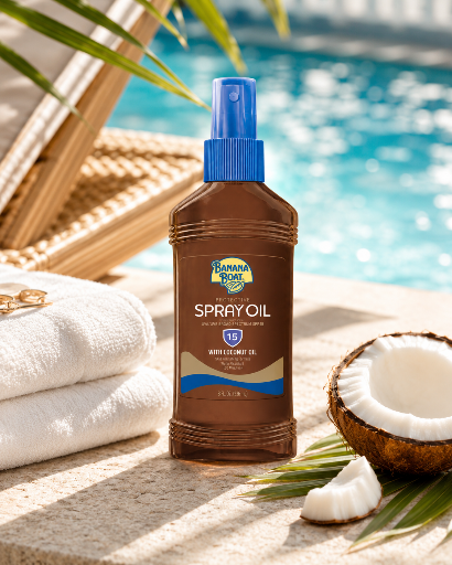 Butelka sprayu do opalania Banana Boat SPF 15 z olejkiem kokosowym stoi na kamiennej powierzchni obok ręczników i otwartego kokosa, w tle widać basen.