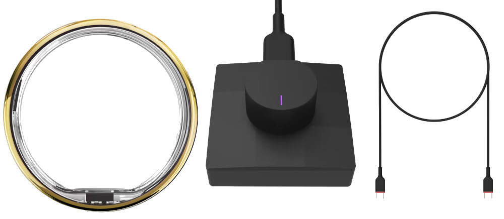 Obraz przedstawia złoty pierścień, czarną stację ładującą z podłączonym kablem oraz osobny kabel z końcówkami USB.